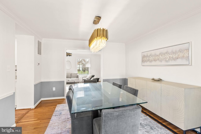 dining space featuring a notable chandelier, light wood finished floors, visible vents, ornamental molding, and baseboards