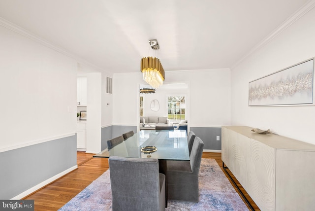 dining space featuring a chandelier, wood finished floors, visible vents, baseboards, and crown molding