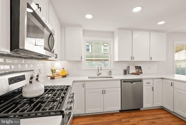 kitchen featuring white cabinets, appliances with stainless steel finishes, wood finished floors, light countertops, and a sink