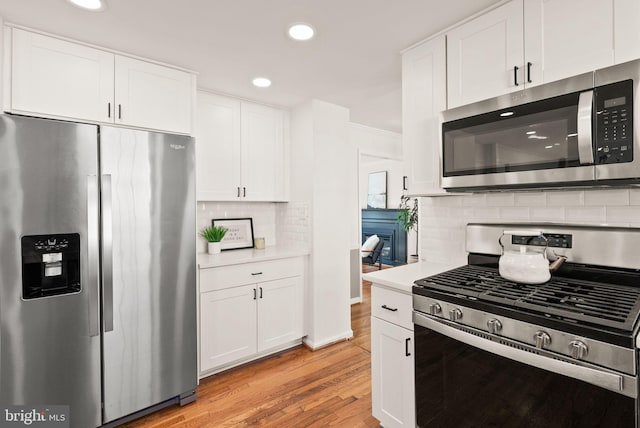 kitchen with light wood finished floors, white cabinets, decorative backsplash, stainless steel appliances, and light countertops