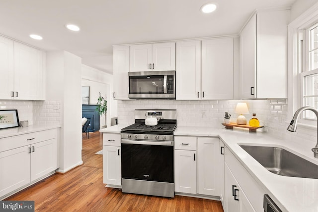 kitchen featuring stainless steel appliances, light countertops, light wood-style floors, white cabinetry, and a sink