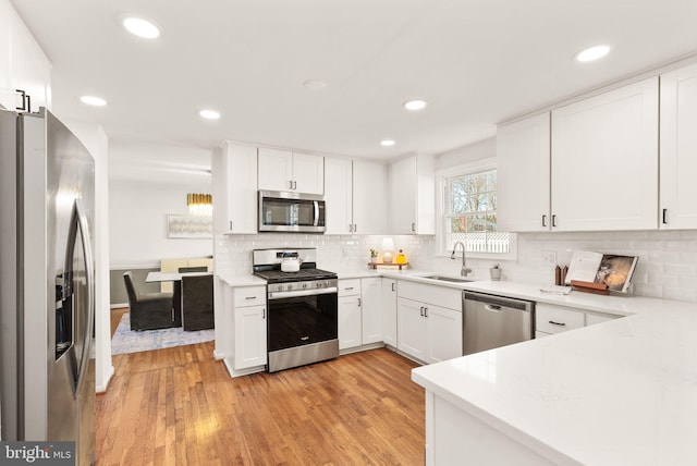 kitchen with a sink, white cabinetry, light wood-style floors, appliances with stainless steel finishes, and decorative backsplash