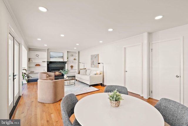 dining room featuring light wood finished floors, ornamental molding, and a glass covered fireplace