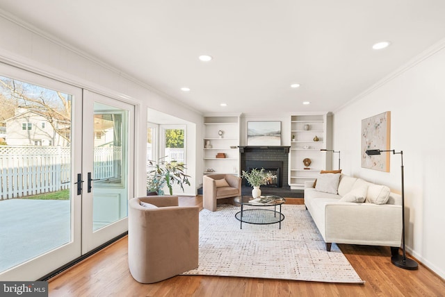 living room with a fireplace, wood finished floors, crown molding, and french doors