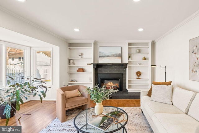 living room with built in shelves, wood finished floors, baseboards, ornamental molding, and a brick fireplace