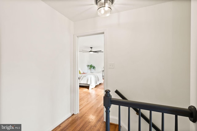 hall with baseboards, an upstairs landing, and wood finished floors