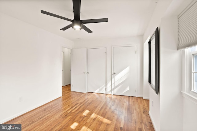 unfurnished bedroom featuring baseboards, ceiling fan, light wood finished floors, and two closets