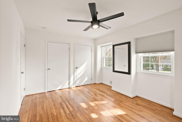 unfurnished bedroom with light wood finished floors, multiple windows, multiple closets, and baseboards