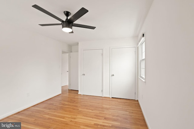 unfurnished bedroom with multiple closets, baseboards, light wood finished floors, and a ceiling fan