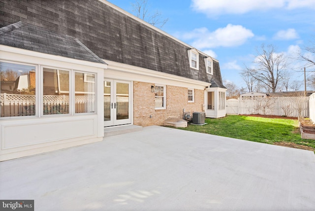 rear view of property featuring brick siding, a patio, mansard roof, a shingled roof, and fence