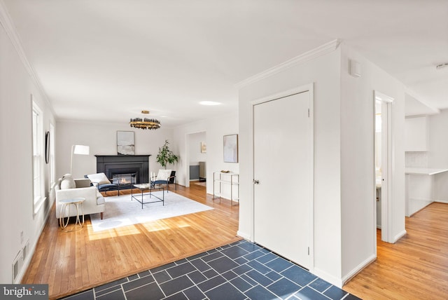 interior space featuring visible vents, baseboards, a glass covered fireplace, wood finished floors, and crown molding