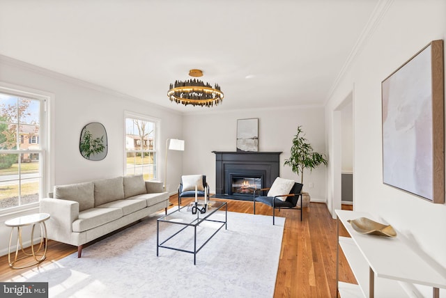 living room with ornamental molding, a glass covered fireplace, baseboards, and wood finished floors