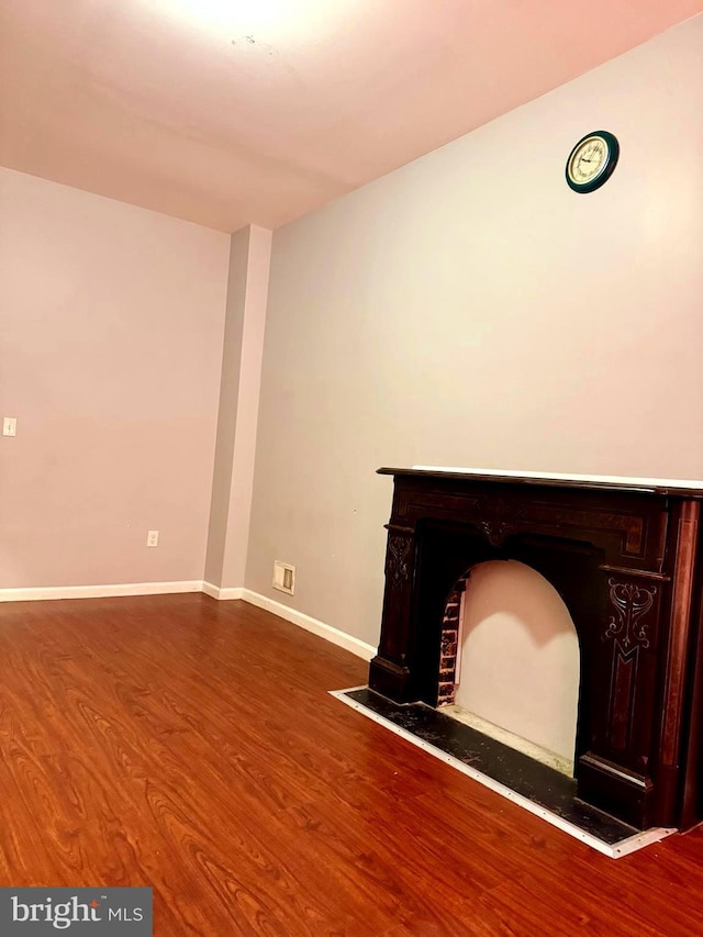 unfurnished living room with baseboards, visible vents, a fireplace with flush hearth, and wood finished floors