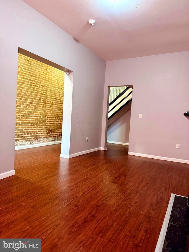 unfurnished room with baseboards, wood finished floors, and brick wall