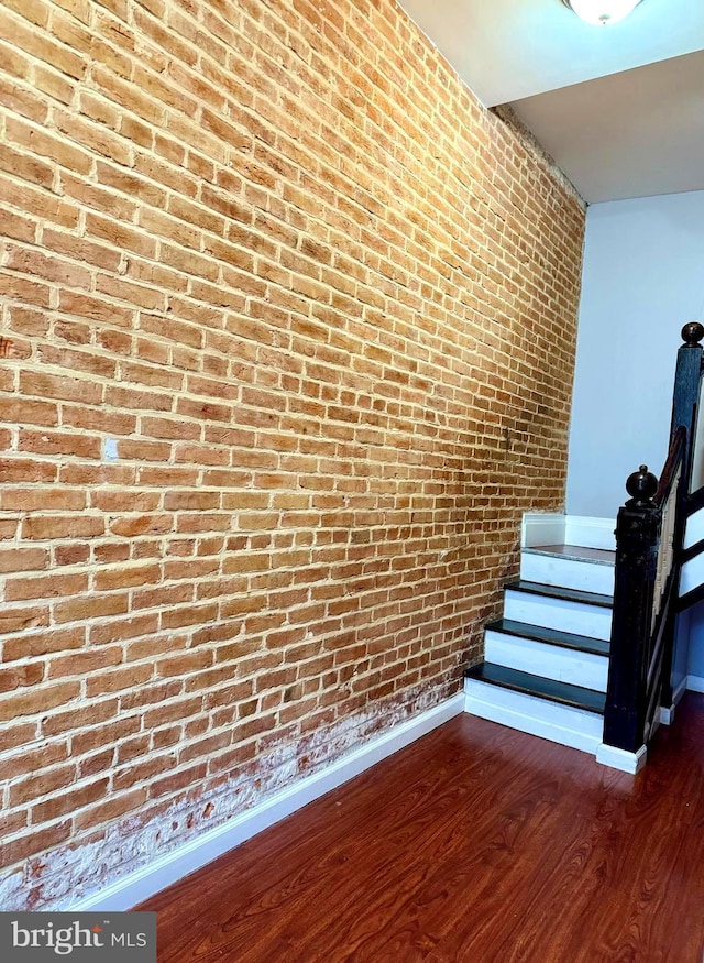 stairway featuring brick wall, baseboards, and wood finished floors
