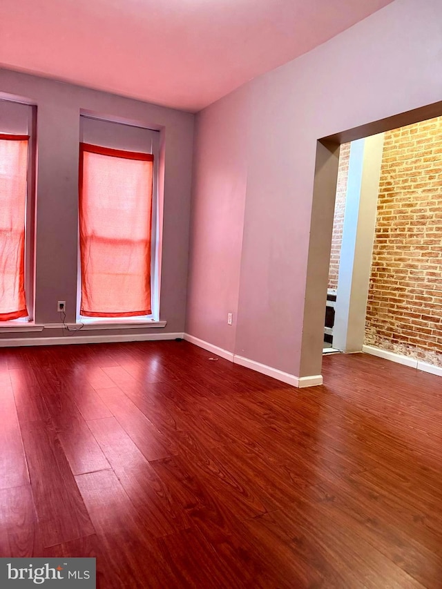 unfurnished room with baseboards, wood finished floors, and brick wall