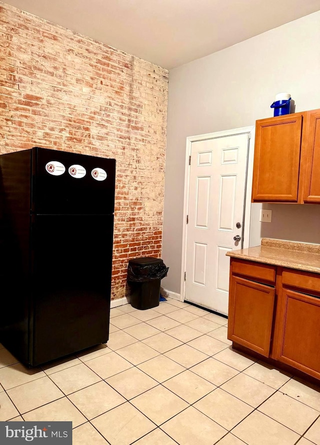 kitchen featuring light countertops, brown cabinets, brick wall, and freestanding refrigerator
