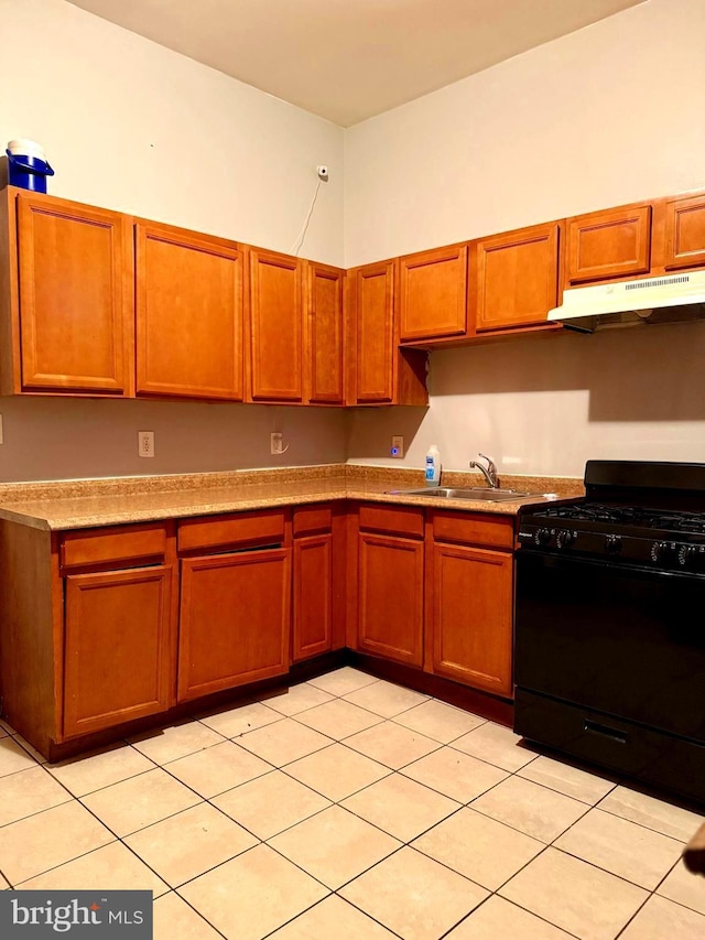 kitchen with light countertops, black range with gas cooktop, under cabinet range hood, a sink, and brown cabinetry