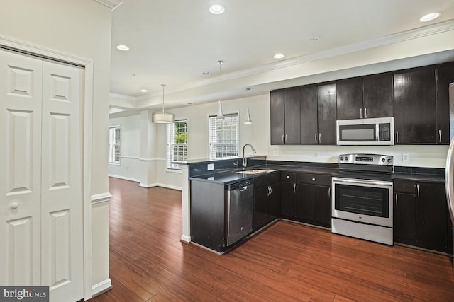 kitchen with sink, dark wood-type flooring, appliances with stainless steel finishes, decorative light fixtures, and kitchen peninsula