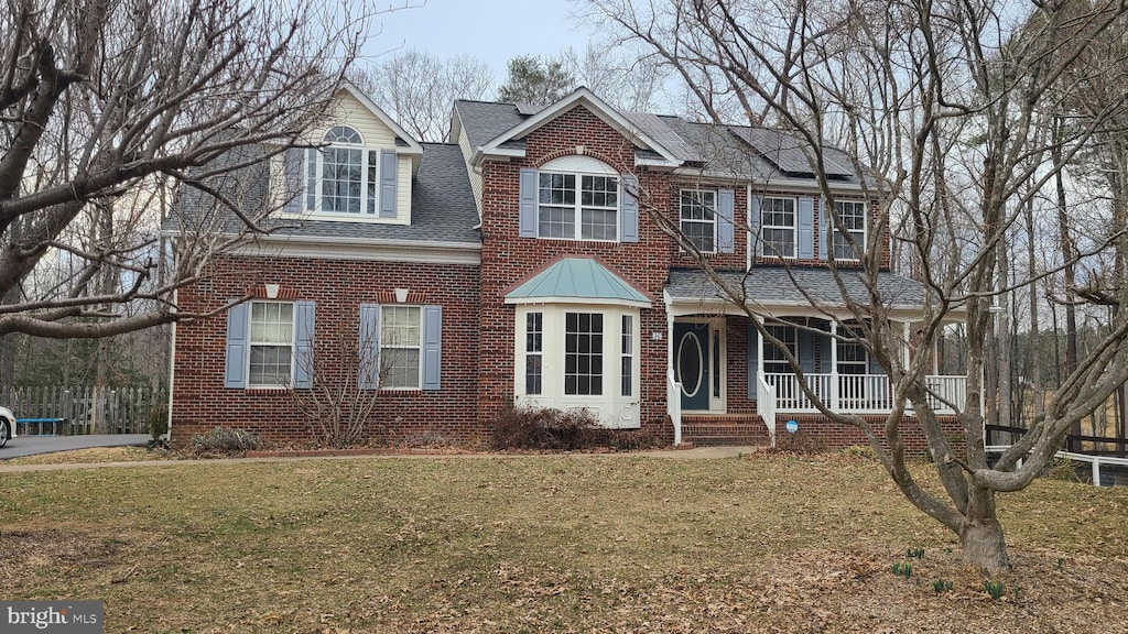 view of front of property with brick siding, covered porch, solar panels, and a front yard