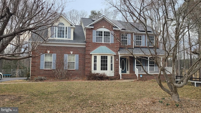 view of front of property with brick siding, covered porch, solar panels, and a front yard