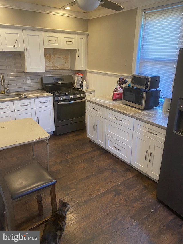 kitchen featuring dark wood-style floors, crown molding, appliances with stainless steel finishes, wainscoting, and white cabinetry