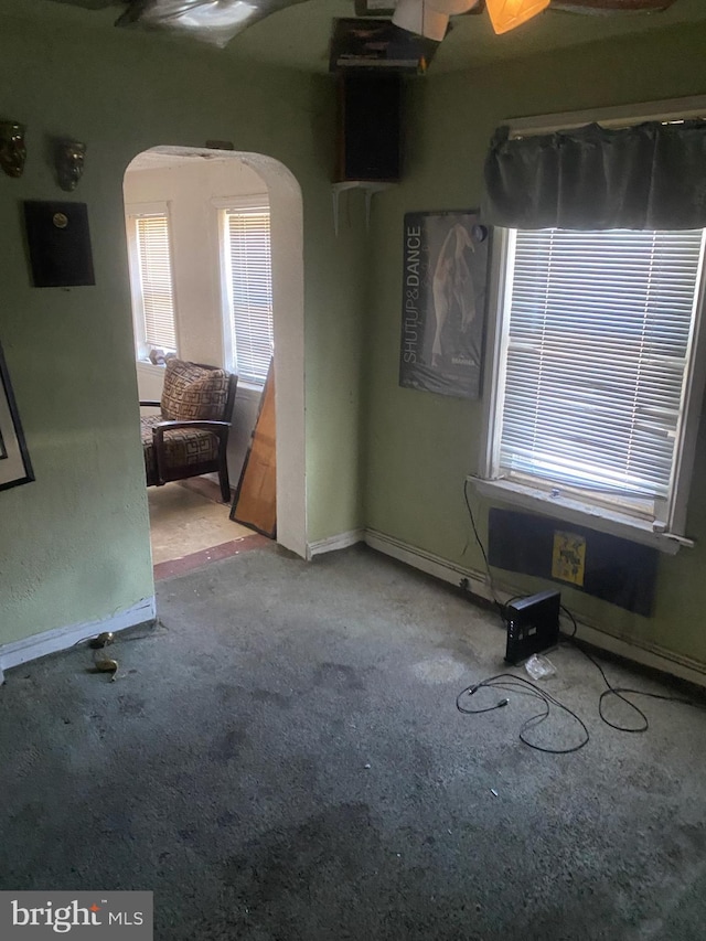 empty room with arched walkways, light carpet, and baseboards