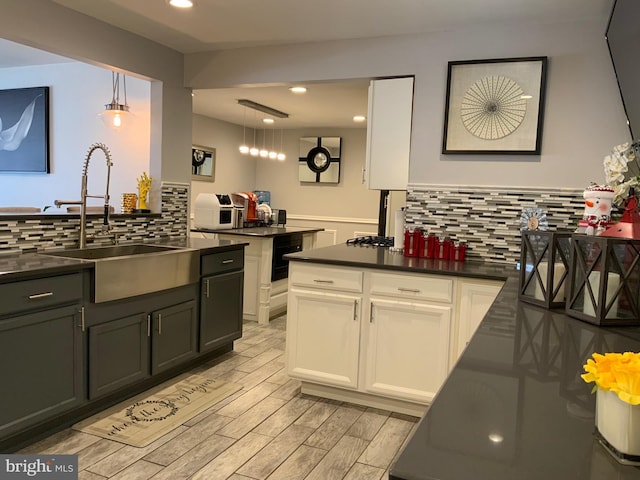 kitchen featuring dark countertops, a sink, white cabinets, and hanging light fixtures