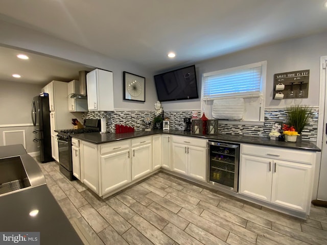 kitchen with dark countertops, white cabinetry, black appliances, beverage cooler, and wall chimney exhaust hood