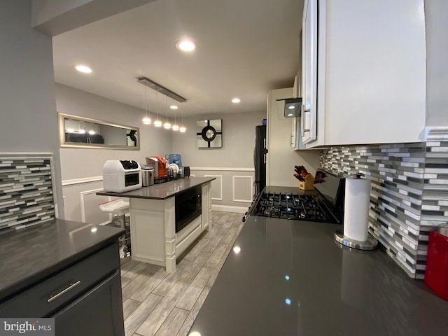 kitchen with a center island, dark countertops, hanging light fixtures, gas stove, and white cabinetry