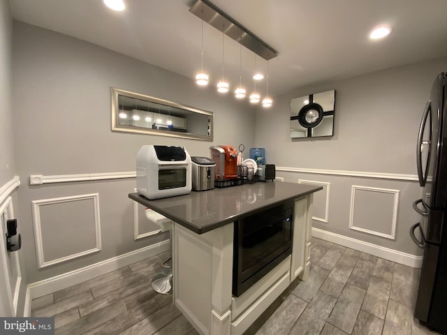 kitchen featuring white cabinets, dark countertops, a breakfast bar, freestanding refrigerator, and pendant lighting