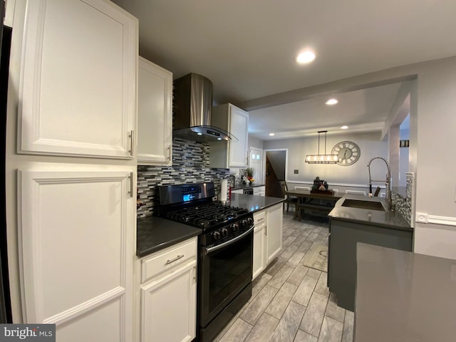 kitchen featuring dark countertops, white cabinets, black range with gas cooktop, wall chimney range hood, and a sink