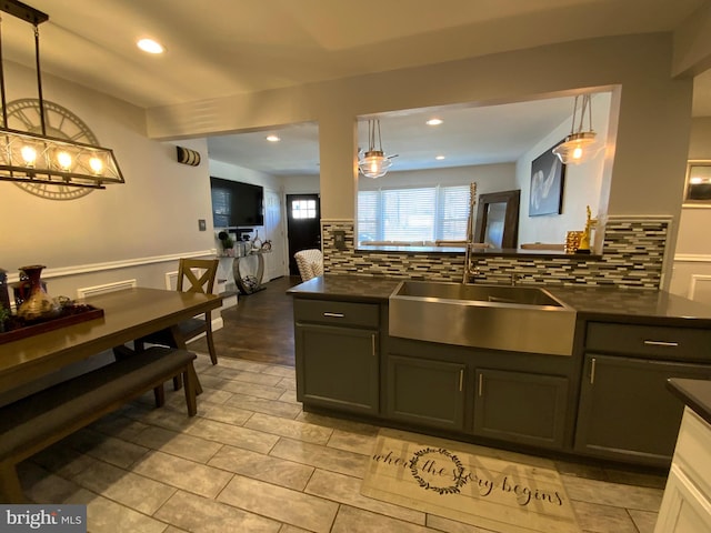 kitchen featuring backsplash, dark countertops, a sink, and pendant lighting