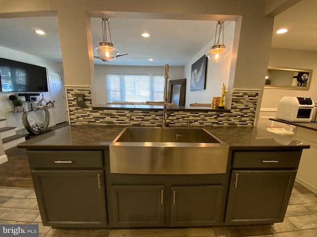 kitchen with hanging light fixtures, backsplash, dark countertops, and a sink