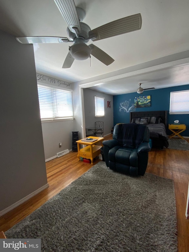 living room with a ceiling fan, visible vents, baseboards, and wood finished floors