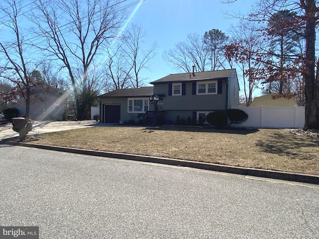 tri-level home with a garage, driveway, a front lawn, and fence