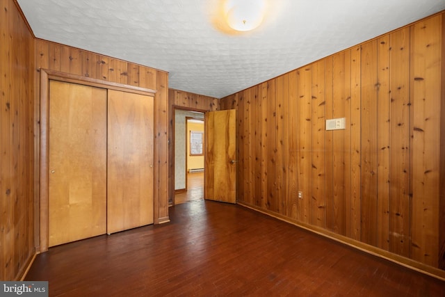 unfurnished bedroom with dark wood-style flooring, a baseboard radiator, a closet, and wooden walls