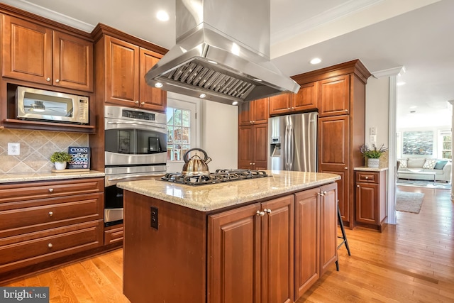 kitchen with stainless steel appliances, island exhaust hood, decorative backsplash, light hardwood / wood-style floors, and a center island