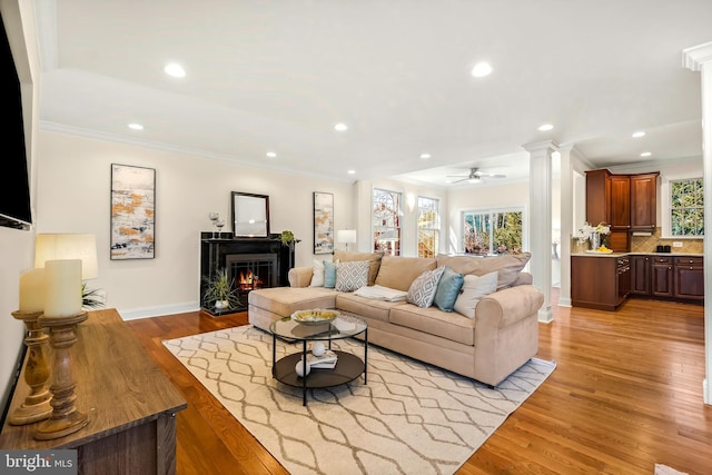 living room featuring ceiling fan, light hardwood / wood-style flooring, crown molding, and decorative columns