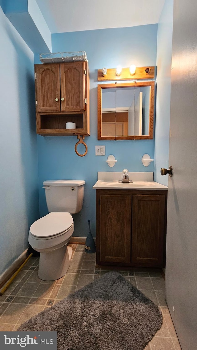 half bath with baseboards, vanity, and toilet