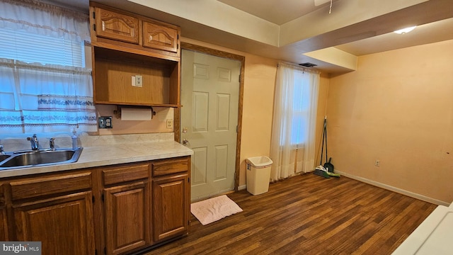 kitchen with a sink, brown cabinets, dark wood-type flooring, light countertops, and visible vents