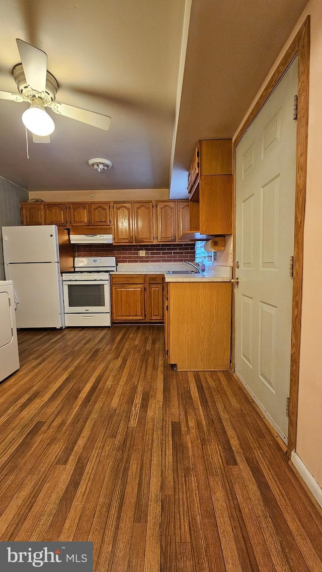 kitchen with under cabinet range hood, light countertops, washer / clothes dryer, white appliances, and dark wood-type flooring