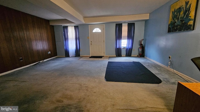 foyer entrance with wooden walls, baseboards, and light carpet