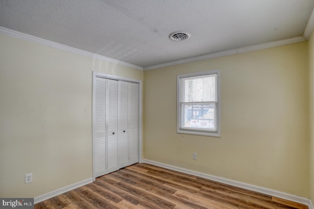 unfurnished bedroom featuring ornamental molding, a textured ceiling, a closet, and hardwood / wood-style floors