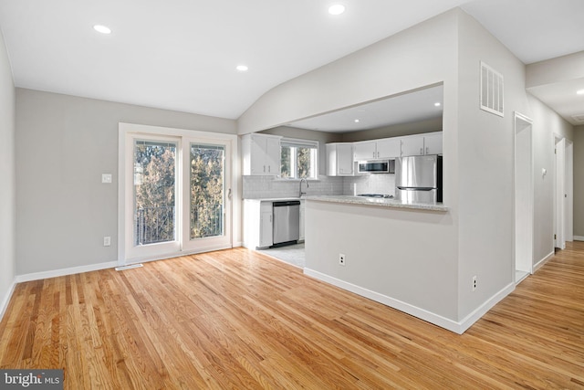 kitchen featuring tasteful backsplash, stainless steel appliances, white cabinets, lofted ceiling, and light wood-type flooring