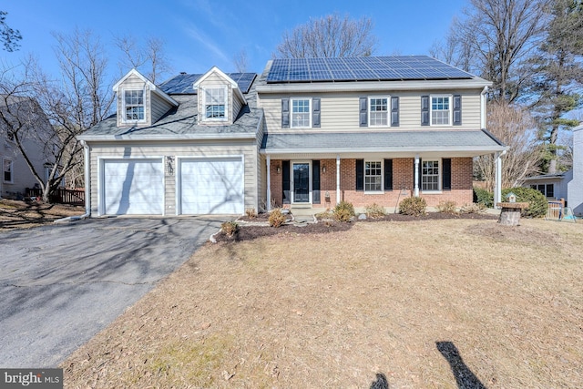 traditional-style house featuring driveway, an attached garage, roof mounted solar panels, a porch, and brick siding