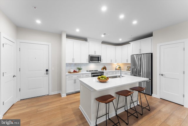 kitchen featuring a sink, white cabinets, light countertops, appliances with stainless steel finishes, and a center island with sink