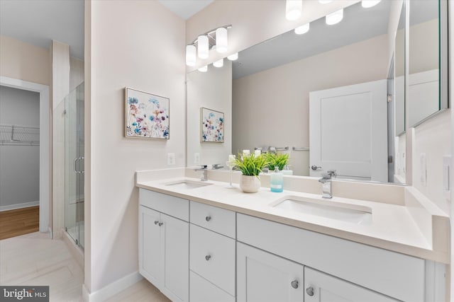 full bathroom with a walk in closet, a sink, a shower stall, and double vanity