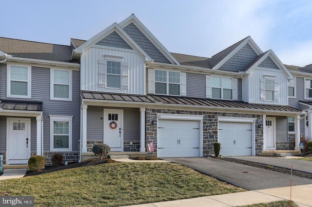 view of property with stone siding, driveway, an attached garage, and a standing seam roof