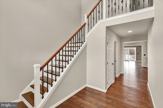 staircase featuring a towering ceiling, baseboards, and wood finished floors